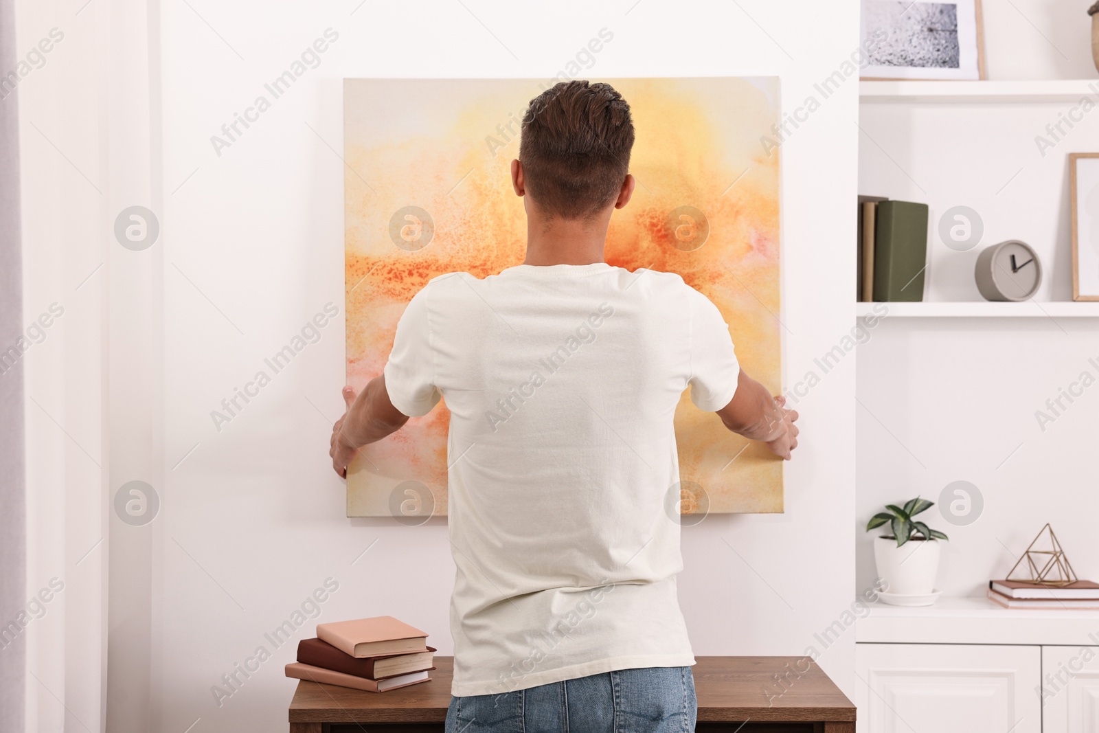 Photo of Male decorator hanging abstract picture indoors, back view