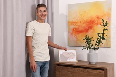 Photo of Smiling young decorator with abstract picture indoors