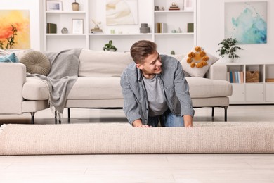 Photo of Happy decorator rolling out beige carpet indoors