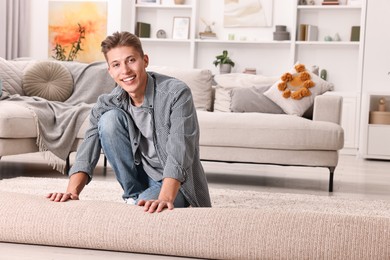 Photo of Happy decorator rolling out beige carpet indoors