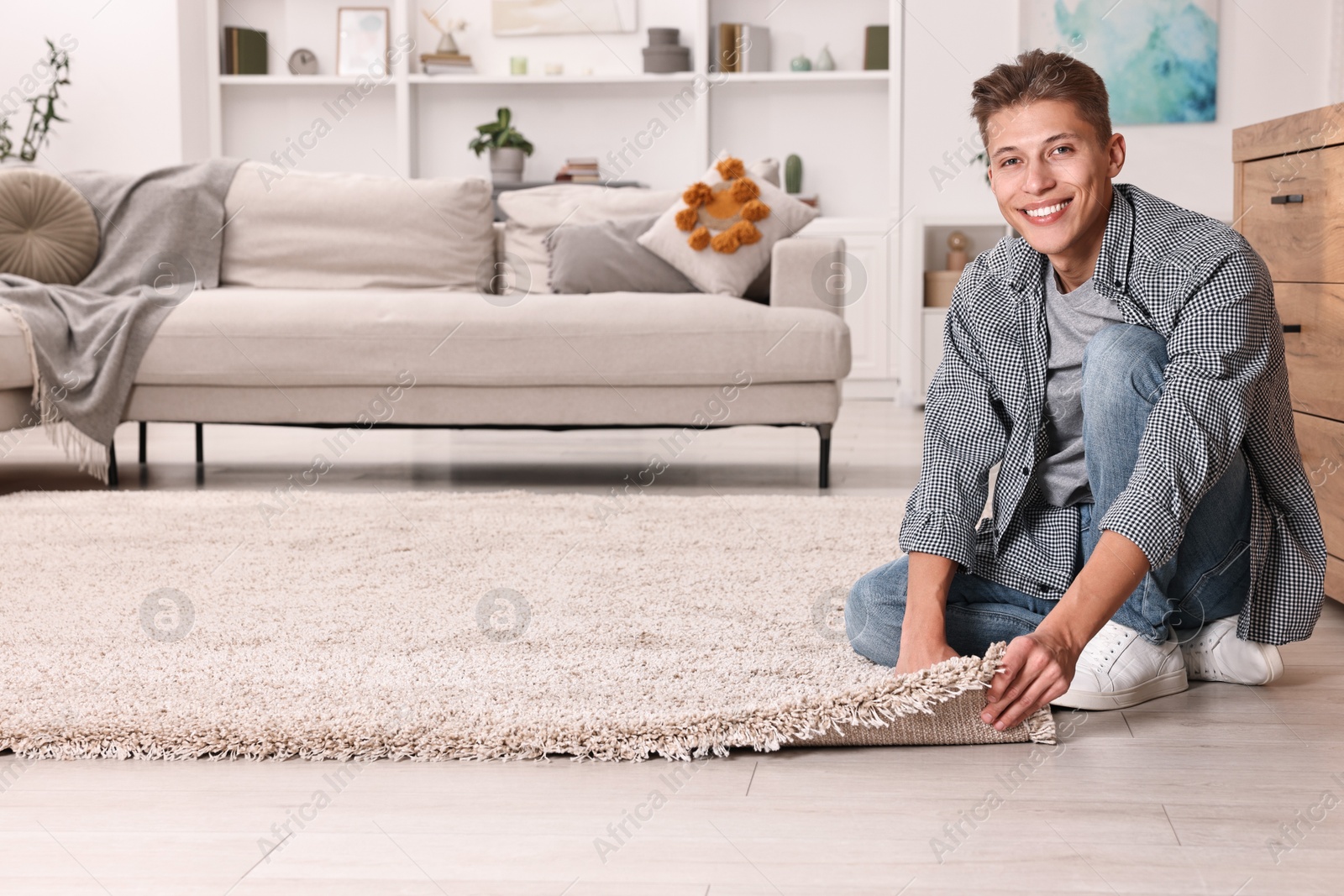 Photo of Smiling decorator placing beige carpet indoors. Space for text