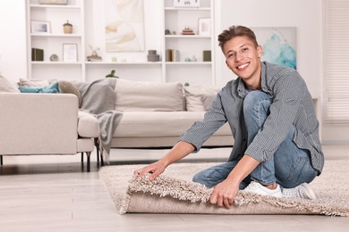 Photo of Smiling decorator placing beige carpet indoors. Space for text