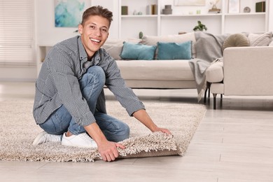 Photo of Smiling decorator placing beige carpet indoors. Space for text