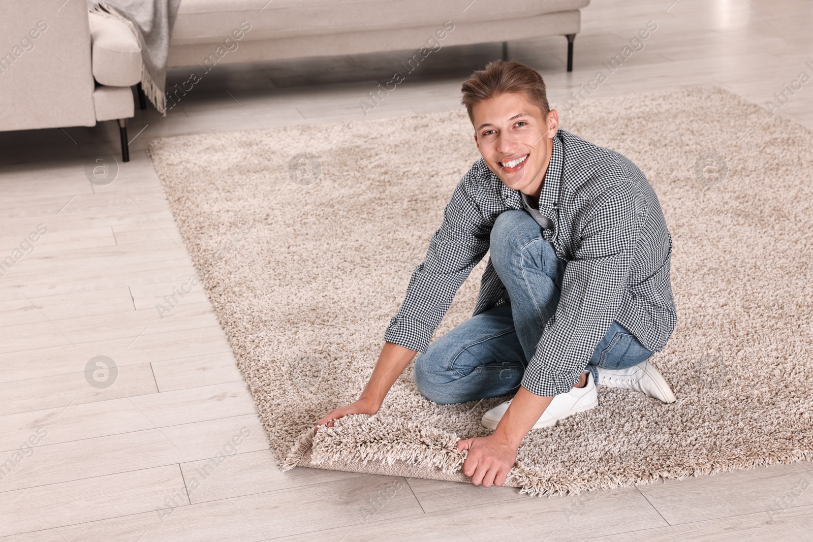 Photo of Smiling decorator placing beige carpet indoors. Space for text