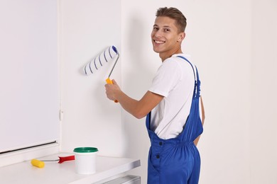 Photo of Smiling handyman painting wall with roller indoors