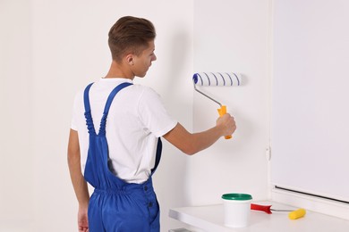 Photo of Male handyman painting wall with roller indoors