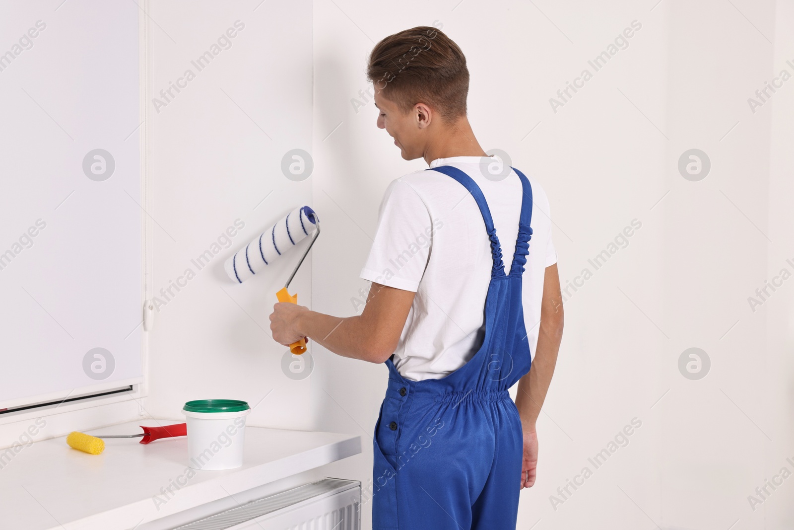 Photo of Male handyman painting wall with roller indoors