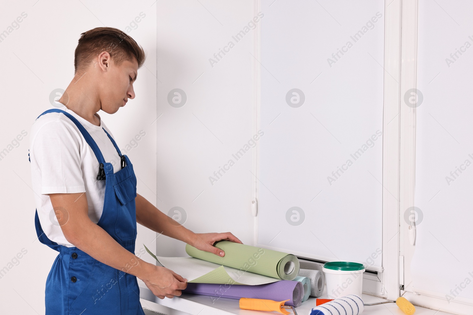 Photo of Male handyman with wallpapers and paint roller at window sill indoors