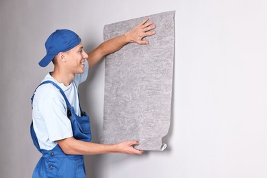 Photo of Smiling handyman hanging grey wallpaper on wall indoors