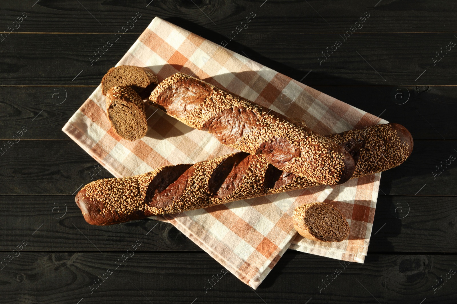 Photo of Fresh baguettes with sesame on black wooden table, flat lay