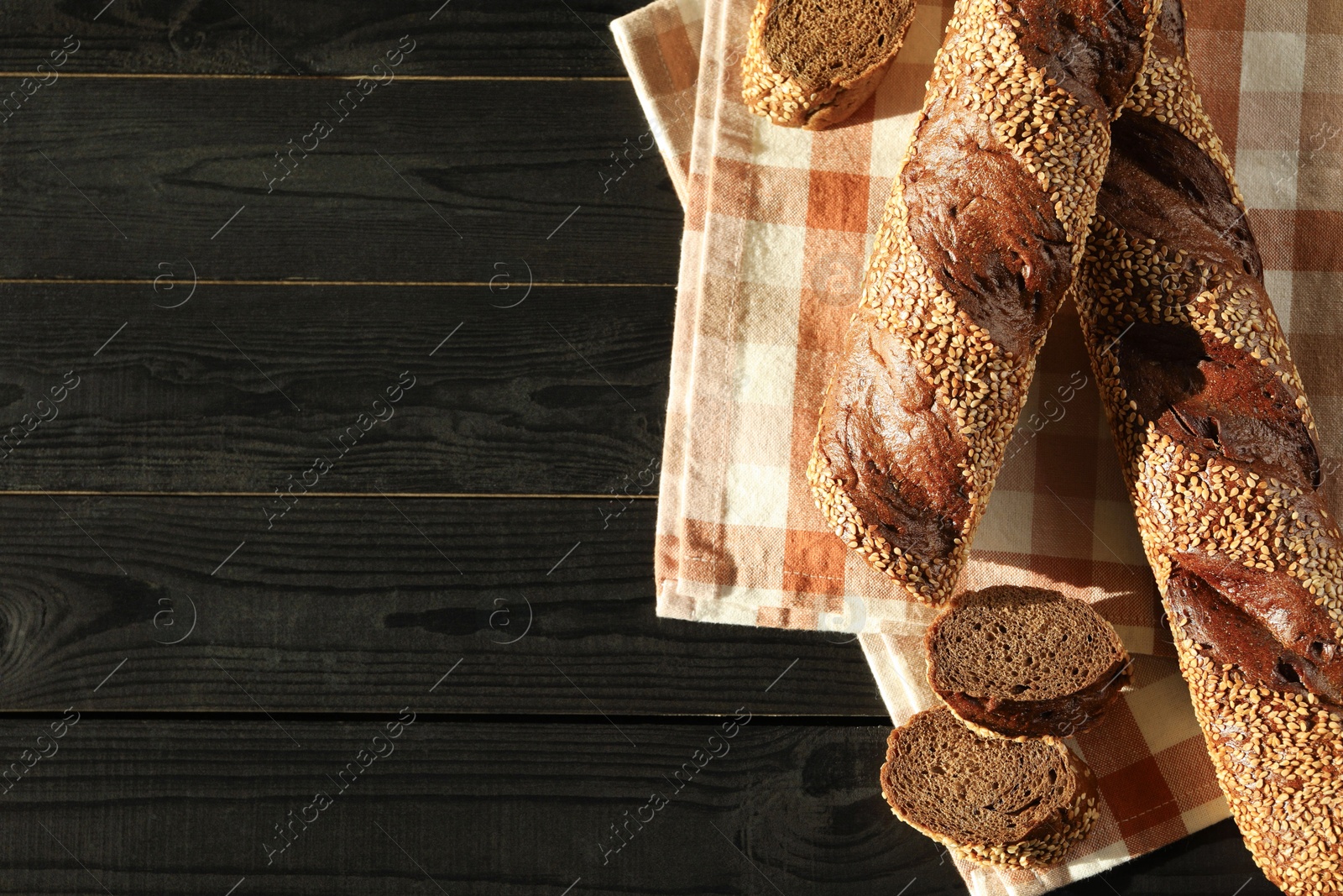 Photo of Fresh baguettes with sesame on black wooden table, flat lay. Space for text