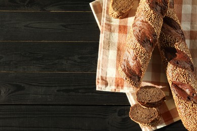 Fresh baguettes with sesame on black wooden table, flat lay. Space for text