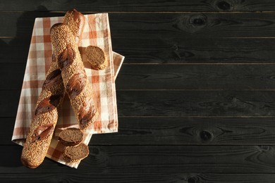 Photo of Fresh baguettes with sesame on black wooden table, flat lay. Space for text