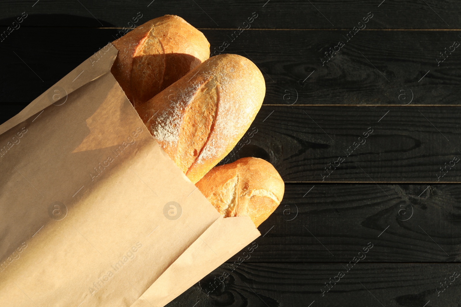 Photo of Fresh baguettes in paper bag on black wooden table, top view. Space for text