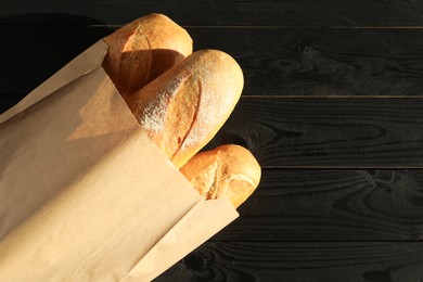 Photo of Fresh baguettes in paper bag on black wooden table, top view. Space for text