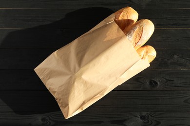 Photo of Fresh baguettes in paper bag on black wooden table, top view