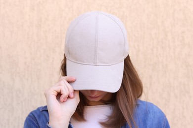 Photo of Woman in stylish baseball cap near beige wall. Mockup for design