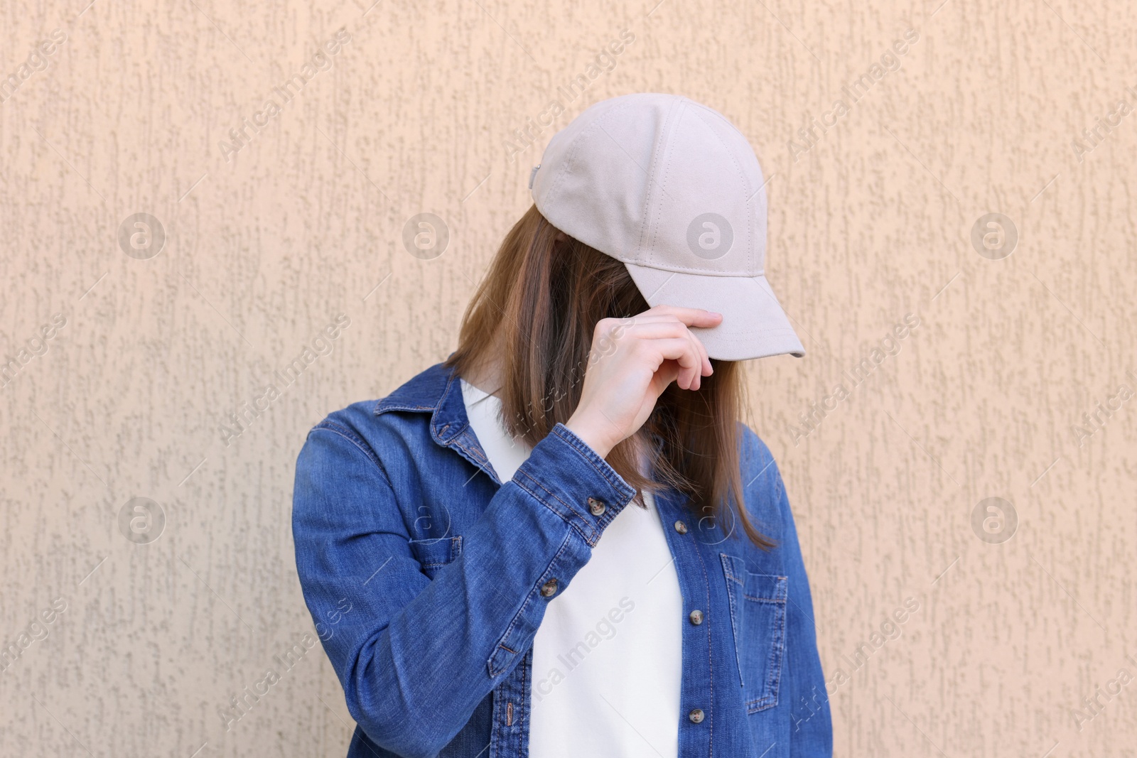 Photo of Woman in stylish baseball cap near beige wall. Mockup for design