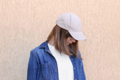 Photo of Woman in stylish baseball cap near beige wall. Mockup for design