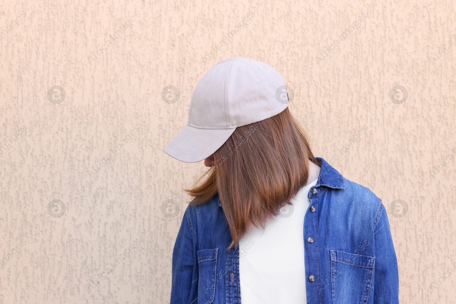 Photo of Woman in stylish baseball cap near beige wall. Mockup for design