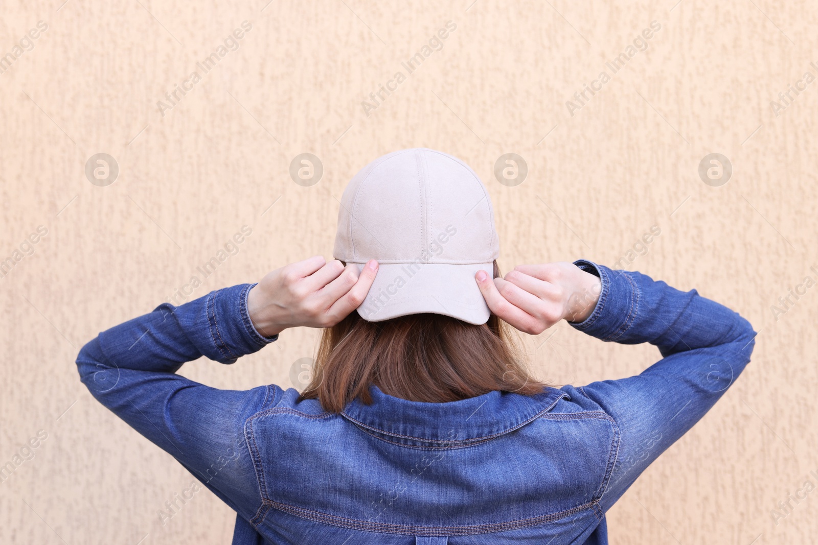 Photo of Woman in stylish baseball cap near beige wall, back view. Mockup for design