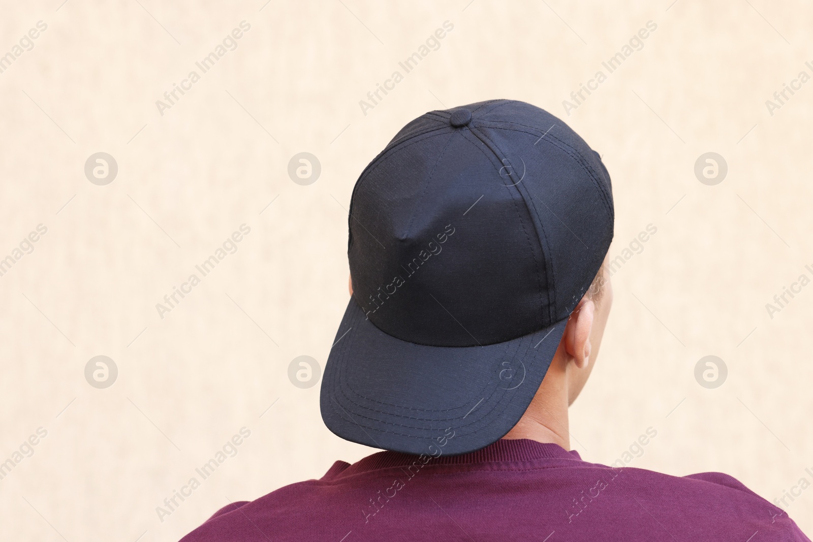 Photo of Man in stylish baseball cap near beige wall, back view. Mockup for design