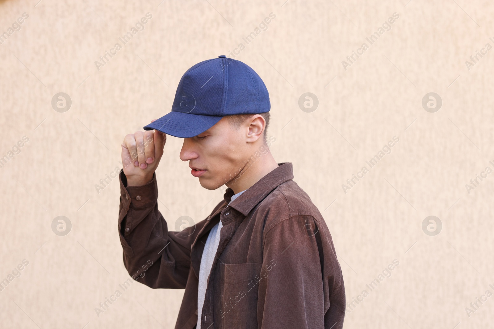 Photo of Man in stylish baseball cap near beige wall. Mockup for design