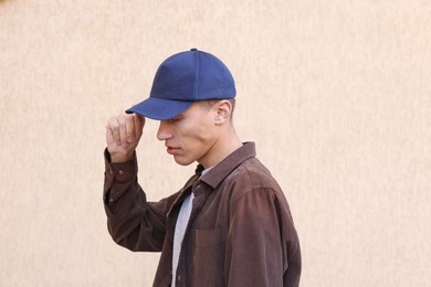 Photo of Man in stylish baseball cap near beige wall. Mockup for design