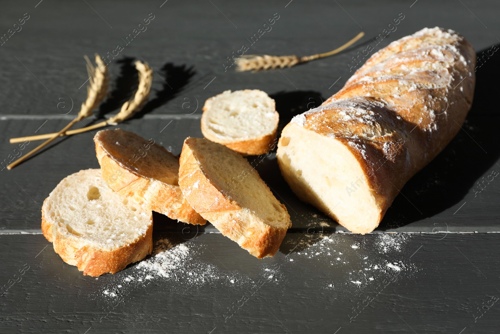 Photo of Pieces of fresh baguette with flour and spikes on grey wooden table