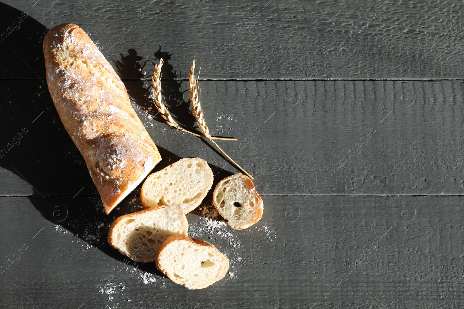 Photo of Pieces of fresh baguette with flour and spikes on grey wooden table, flat lay. Space for text