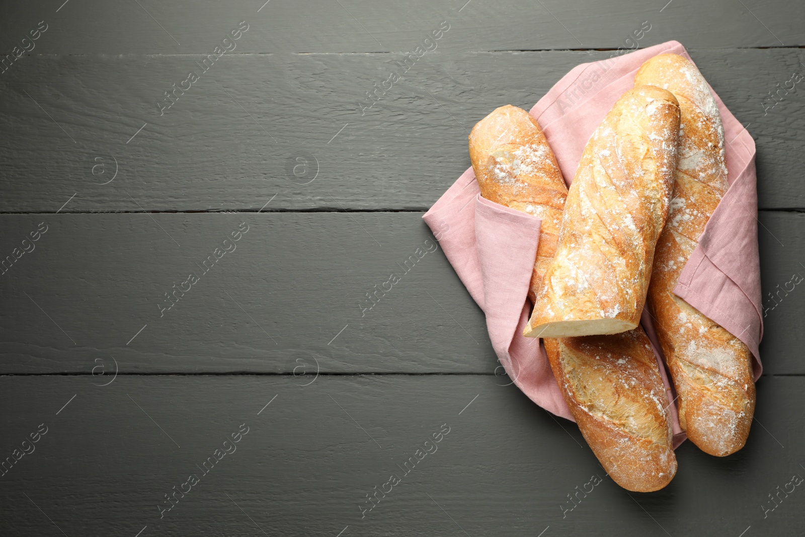 Photo of Cut fresh baguettes on grey wooden table, top view. Space for text