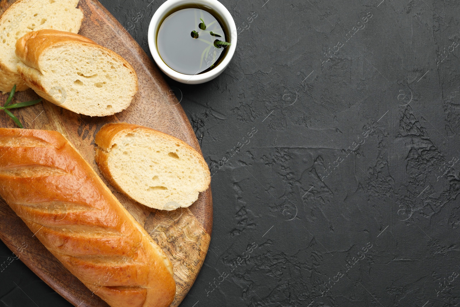 Photo of Cut fresh baguette with balsamic and rosemary on black table, top view. Space for text