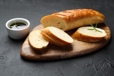 Photo of Cut fresh baguette with balsamic and rosemary on black table, closeup