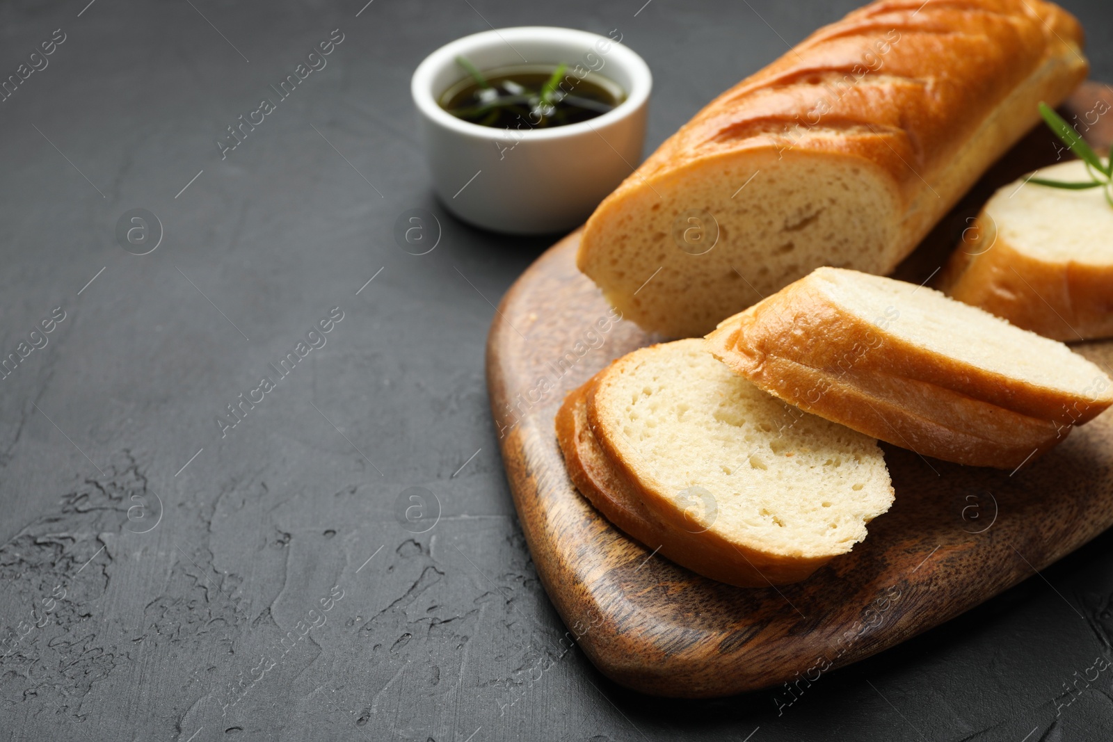 Photo of Cut fresh baguette with balsamic on black table, closeup. Space for text