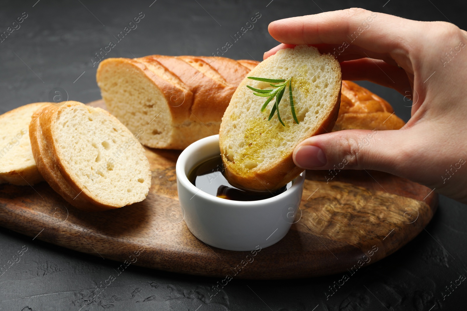 Photo of Woman dipping slice of tasty baguette into balsamic at black table, closeup