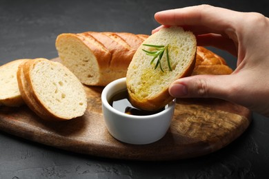 Photo of Woman dipping slice of tasty baguette into balsamic at black table, closeup