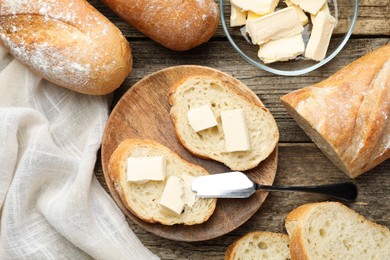 Photo of Slices of fresh baguette with butter on wooden table, flat lay