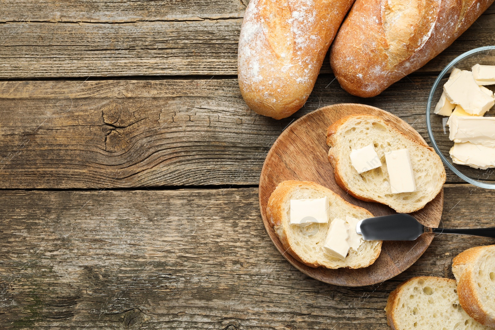 Photo of Slices of fresh baguette with butter on wooden table, flat lay. Space for text