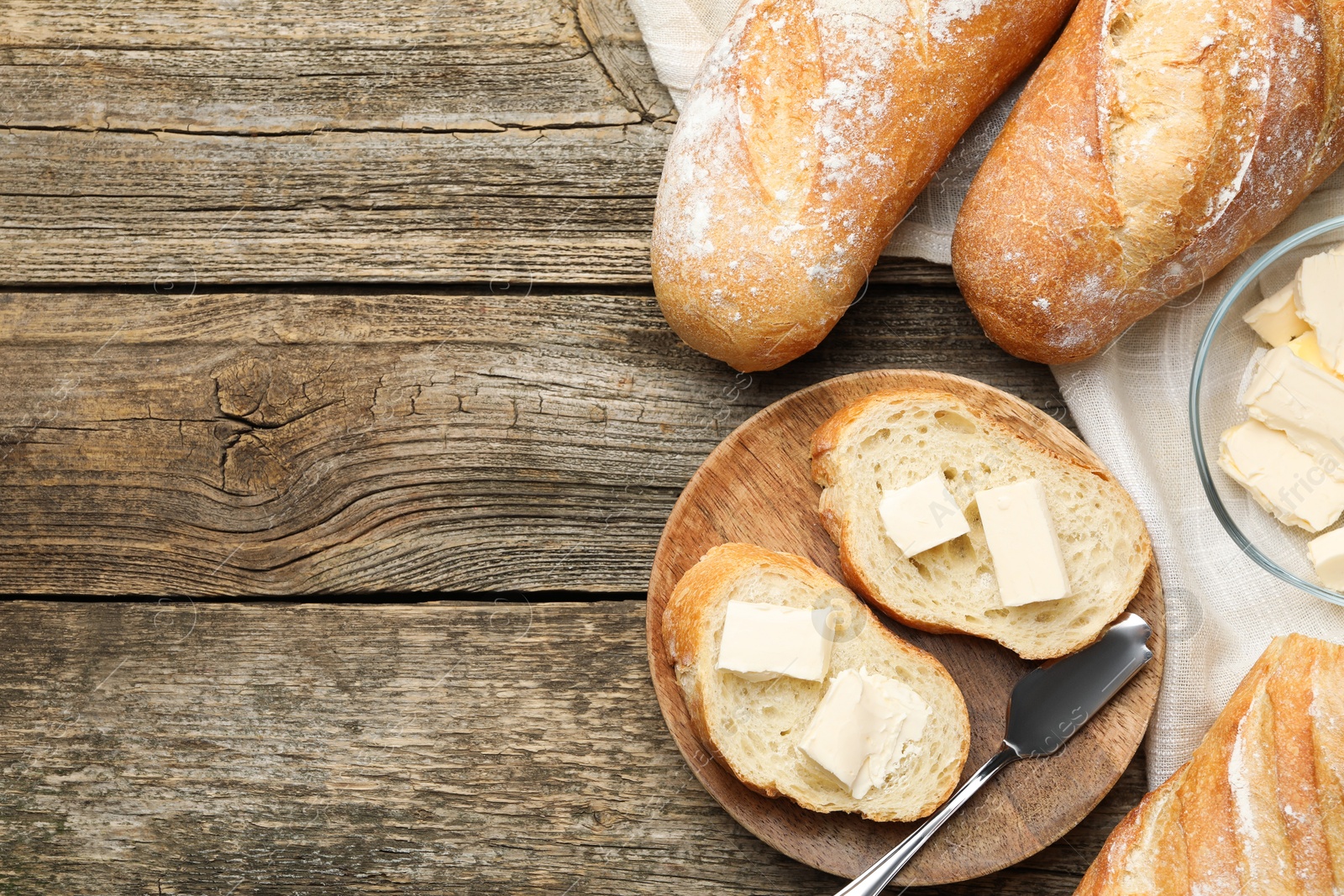 Photo of Slices of fresh baguette with butter on wooden table, flat lay. Space for text