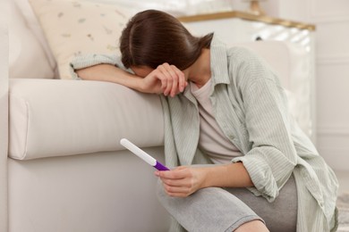 Photo of Upset woman with negative pregnancy test at home