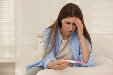 Photo of Upset woman with negative pregnancy test on sofa at home, space for text