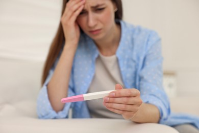 Photo of Upset woman with negative pregnancy test on sofa at home, selective focus