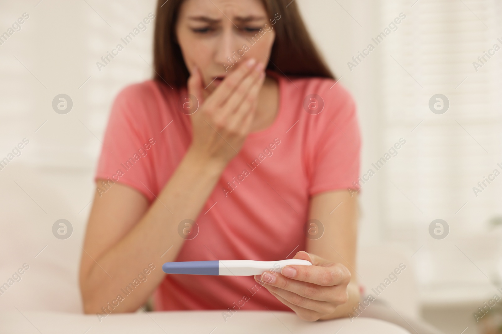 Photo of Upset woman with negative pregnancy test at home, selective focus