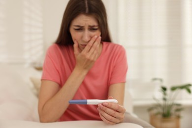 Photo of Upset woman with negative pregnancy test on sofa at home, selective focus. Space for text