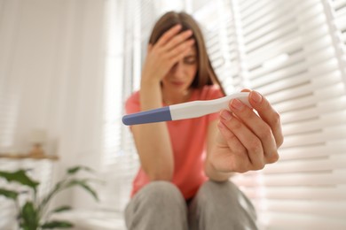 Photo of Upset woman with negative pregnancy test near window at home, selective focus