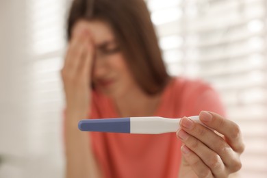 Photo of Upset woman with negative pregnancy test at home, selective focus