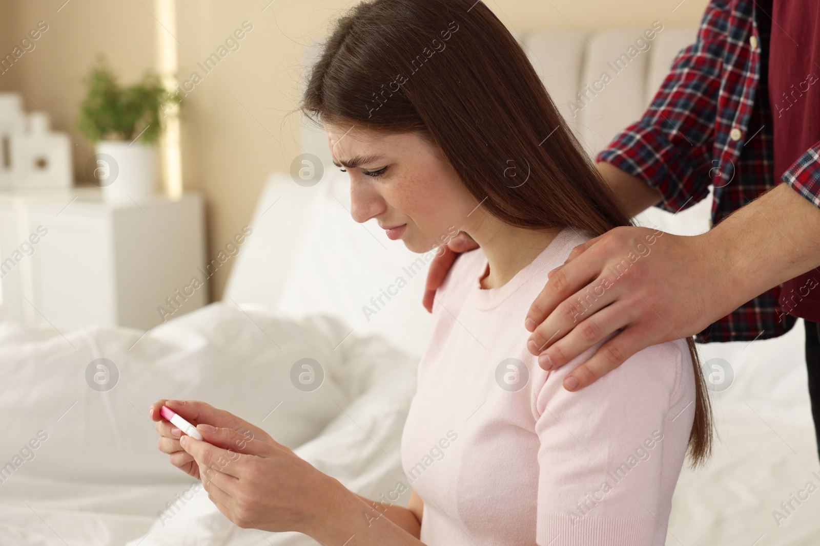 Photo of Upset woman with negative pregnancy test indoors. Man supporting his wife at home