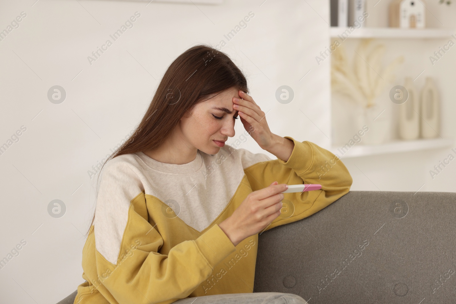 Photo of Upset woman with negative pregnancy test on sofa at home