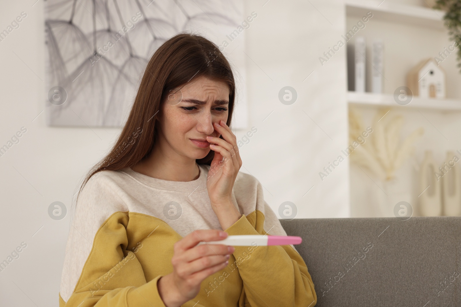 Photo of Upset woman with negative pregnancy test on sofa at home