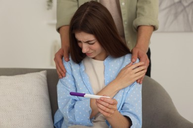 Photo of Upset woman with negative pregnancy test indoors. Man supporting his wife at home